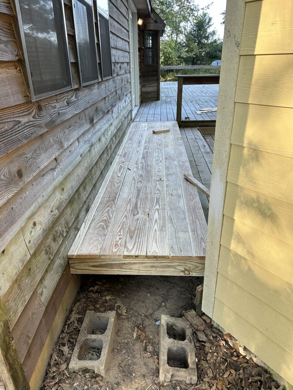 Wooden ramp leading to a deck between two buildings, supported by concrete blocks.